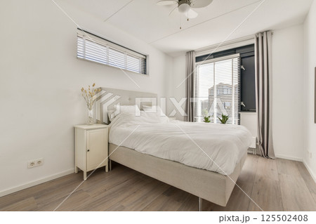 A serene and stylish bedroom featuring a neutral color palette, large windows for natural light, and minimalist decor that promotes relaxation. 125502408