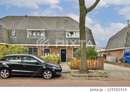 A contemporary residential structure featuring a sleek design, equipped with a parked car and greenery surrounding it, set in a peaceful neighborhood. 125502414