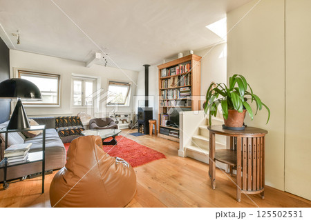 A stylish and inviting living room featuring a mix of modern furniture and natural light, accented by indoor plants and warm wooden flooring. 125502531