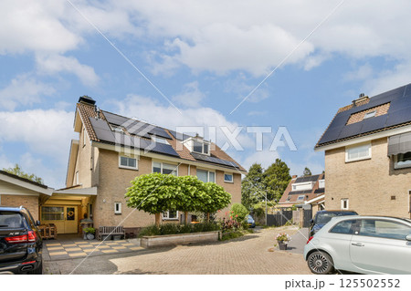 A contemporary house featuring solar panels, a manicured garden, and a clear blue sky, showcasing a blend of eco-friendly design and modern architecture. 125502552