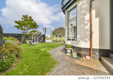 A serene garden featuring lush greenery and a charming brick pathway beside a contemporary home, perfect for outdoor relaxation and landscaping inspiration. 125502554