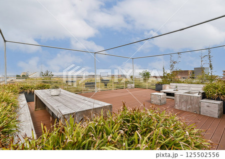 A stylish rooftop garden featuring wooden furniture, lush greenery, and a scenic sky, perfect for relaxation and social gatherings. A stylish rooftop garden featuring wooden furniture, lush greenery, and a scenic sky, perfect for relaxation and social gatherings. 125502556