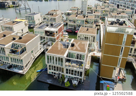 Aerial view of contemporary floating houses arranged near a canal, showcasing innovative architecture and vibrant colors in urban living. Aerial view of contemporary floating houses arranged near a canal, showcasing innovative architecture and vibrant colors in urban living. 125502588