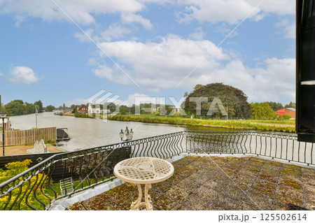 A picturesque view from a balcony overlooking a serene river, surrounded by lush greenery and quaint houses under a cloudy sky. A picturesque view from a balcony overlooking a serene river, surrounded by lush greenery and quaint houses under a cloudy sky. 125502614