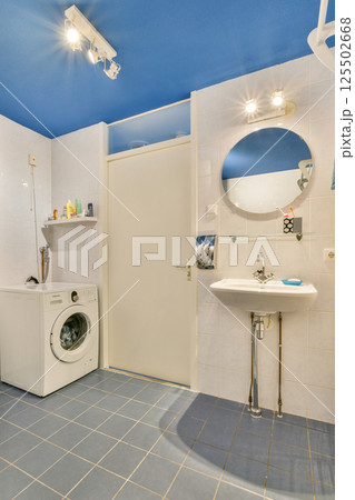 A contemporary laundry room featuring a washing machine, a round mirror, and a bright blue ceiling, designed for functionality and style. A contemporary laundry room featuring a washing machine, a round mirror, and a bright blue ceiling, designed for functionality and style. 125502668
