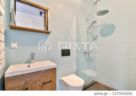 Stylish bathroom design featuring a glass shower enclosure, minimalist furnishings, and soothing blue wall colors. Ideal for contemporary home aesthetic. 125502692