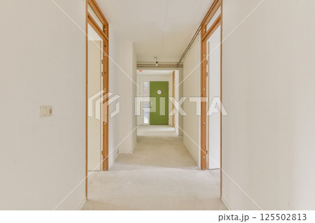 A spacious interior hallway showcasing clean lines, white walls, and wooden trims, leading to a vibrant green door. 125502813