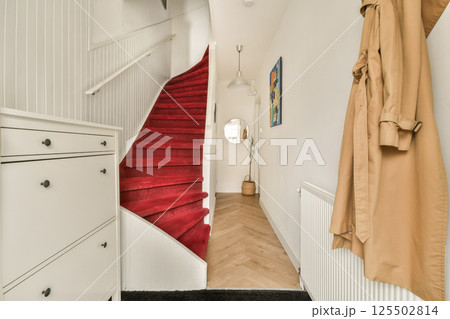 A stylish contemporary staircase adorned with a red carpet, leading up in a well-lit hallway featuring minimalistic decor and elegant furniture. 125502814