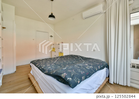 A serene modern bedroom featuring a comfortable bed, soft linens, and minimalistic decor, complemented by natural light from a window. 125502844
