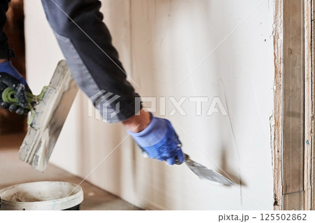 A metal spatula lines the wall with plaster. Apartment renovation. Leveling the plastered wall. With space to copy. High quality photo A metal spatula lines the wall with plaster. Apartment renovation. Leveling the plastered wall. With space to copy. High quality photo 125502862