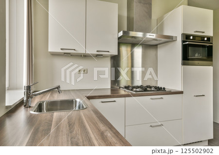 This sleek kitchen features a contemporary layout with a minimalist design, clean lines, and elegant cabinetry. Ideal for functional cooking and style. 125502902