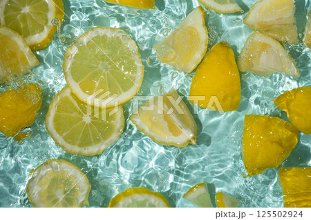 Refreshing turquoise citrus background with floating yellow lemon pieces Refreshing turquoise citrus background with floating yellow lemon pieces 125502924