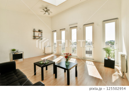 A stylish modern living room featuring large windows that flood the space with natural light, complemented by minimalist furniture and indoor plants. A stylish modern living room featuring large windows that flood the space with natural light, complemented by minimalist furniture and indoor plants. 125502954