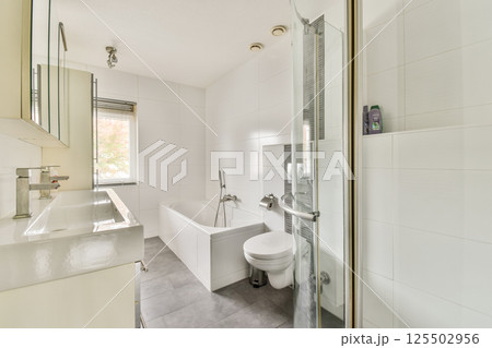 A sleek and contemporary bathroom featuring a bathtub, shower, and minimalist design elements. The tiles and fixtures create a clean and spacious atmosphere. 125502956