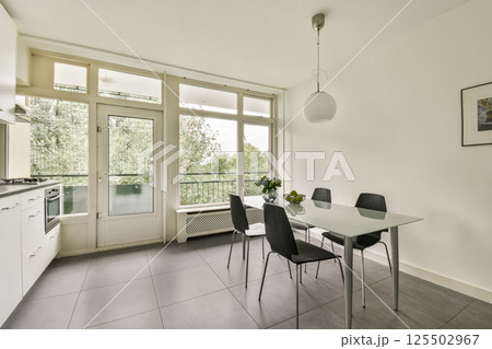 Bright and airy kitchen featuring a sleek design, simple furniture, and a view of nature through large windows, perfect for enjoying meals. 125502967