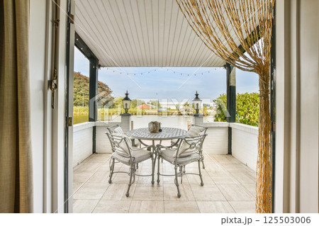 An inviting outdoor patio featuring a round table and chairs, surrounded by lush greenery and decorative lanterns, perfect for relaxation and gatherings. 125503006