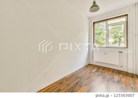 A sparse interior featuring a window that lets in natural light, highlighting the wood floor and clean walls. Ideal for modern design inspiration. 125503007