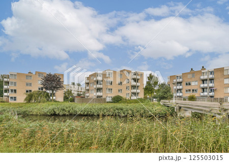 Contemporary apartment complexes surrounded by lush greenery and a calm waterway, showcasing an idyllic living environment amidst nature. 125503015