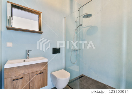 A sleek modern bathroom featuring a glass shower, minimalist sink, and contemporary decor with cool blue walls. 125503054