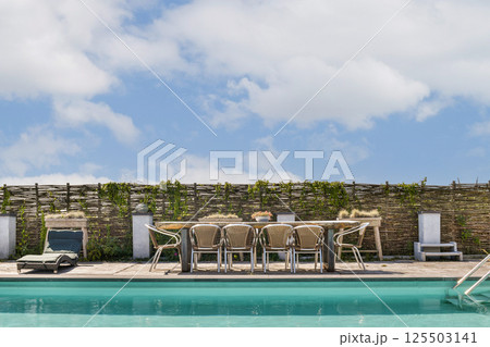 A stylish outdoor patio featuring a swimming pool, wooden fencing, and comfortable seating arrangements under a clear blue sky, perfect for relaxation. A stylish outdoor patio featuring a swimming pool, wooden fencing, and comfortable seating arrangements under a clear blue sky, perfect for relaxation. 125503141