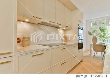 A sleek and stylish modern kitchen featuring beige cabinets, marble countertops, and contemporary lighting creating an inviting atmosphere for cooking and dining. A sleek and stylish modern kitchen featuring beige cabinets, marble countertops, and contemporary lighting creating an inviting atmosphere for cooking and dining. 125503201