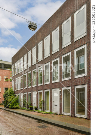 A contemporary residential structure featuring multiple windows and a blend of brick and glass materials, set against a cloudy sky. A contemporary residential structure featuring multiple windows and a blend of brick and glass materials, set against a cloudy sky. 125503325