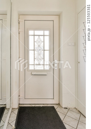 A sleek modern entrance door featuring a glass panel design, accompanied by a large mirror and elegant tile flooring, creating a welcoming ambiance. 125503381