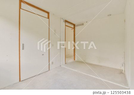 A spacious, empty room featuring clean lines, white walls, and a light floor, perfect for creating a serene environment or an art studio. 125503438