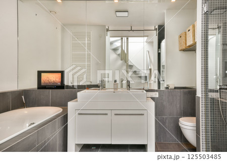 A stylish modern bathroom featuring a sleek bathtub, dual sinks, and a minimalist design with ample natural light creating a luxurious ambiance. 125503485