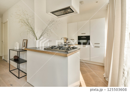 A sleek and contemporary kitchen featuring a gas stove, white cabinets, and natural wood accents. The space is bright and inviting, with minimalist decor. 125503608