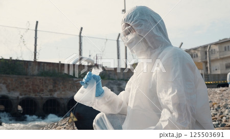 Ecologist sampling water toxic chemicals from river with test tube glass and have white smoke, Biologist wear protective suit and mask collects sample waste water from industrial, problem environment Ecologist sampling water toxic chemicals from river with test tube glass and have white smoke, Biologist wear protective suit and mask collects sample waste water from industrial, problem environment 125503691