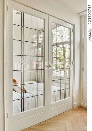 A stylish room featuring elegant glass paneled doors, showcasing a glimpse of natural light and minimalist decor that enhances the contemporary aesthetic. 125503737