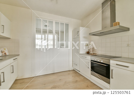 A sleek modern kitchen featuring white cabinetry, a glass door, and stainless steel appliances, creating a bright and spacious cooking space. A sleek modern kitchen featuring white cabinetry, a glass door, and stainless steel appliances, creating a bright and spacious cooking space. 125503761