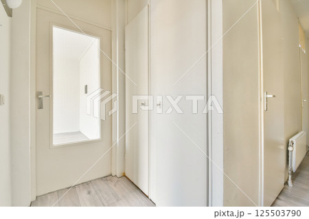 A bright and airy hallway featuring a white door with glass panel, leading to two closed doors, set against a clean and modern aesthetic. 125503790