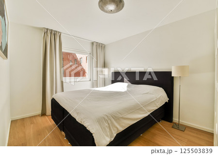 A sleek modern bedroom featuring a light color scheme, large window for natural light, and minimalist decor emphasizing comfort and simplicity. 125503839