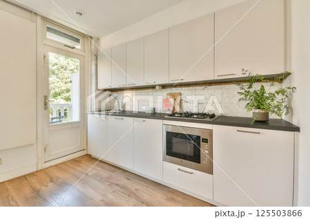 A bright and contemporary kitchen featuring white cabinetry, modern appliances, and a sunny window view. Ideal for cooking and entertaining in style. 125503866