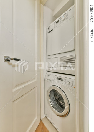 A neatly organized laundry area featuring a stacked washer and dryer tucked away in a built-in closet. The clean lines and bright color create a functional space. A neatly organized laundry area featuring a stacked washer and dryer tucked away in a built-in closet. The clean lines and bright color create a functional space. 125503904