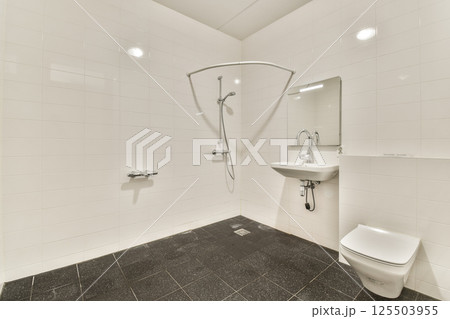 A sleek and minimalist bathroom featuring white tiles, a contemporary shower, sink, and toilet. The clean lines and spacious layout evoke a sense of tranquility. A sleek and minimalist bathroom featuring white tiles, a contemporary shower, sink, and toilet. The clean lines and spacious layout evoke a sense of tranquility. 125503955