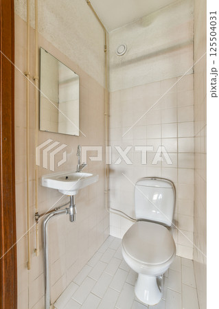 A clean, minimalist bathroom featuring a white toilet, sink, and tiled walls in neutral tones, creating a simple yet functional space. A clean, minimalist bathroom featuring a white toilet, sink, and tiled walls in neutral tones, creating a simple yet functional space. 125504031