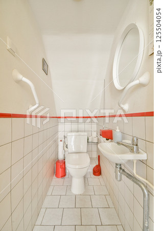 A compact modern bathroom featuring a white toilet, sink, and minimalistic design elements enhanced by a red accent stripe. A compact modern bathroom featuring a white toilet, sink, and minimalistic design elements enhanced by a red accent stripe. 125504054