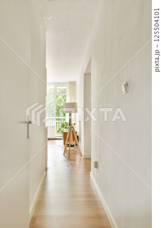 A bright and airy interior hallway featuring a minimalist design with wooden flooring and a modern lamp, inviting natural light from large windows. 125504101