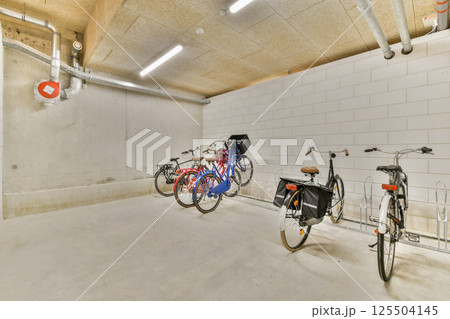 A minimalist garage showcasing various bicycles positioned neatly against a clean, industrial wall with exposed pipes and subtle lighting. 125504145