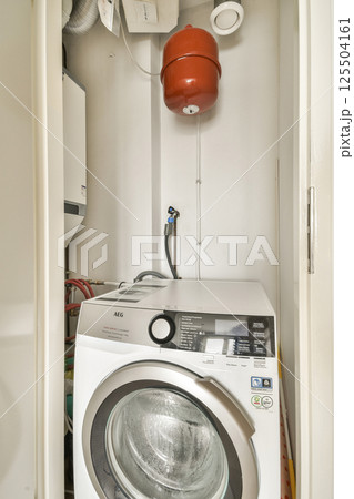 A clean and organized laundry room featuring a washing machine, with plumbing visible and a fire extinguisher hanging on the wall. Ideal for practical home designs. 125504161