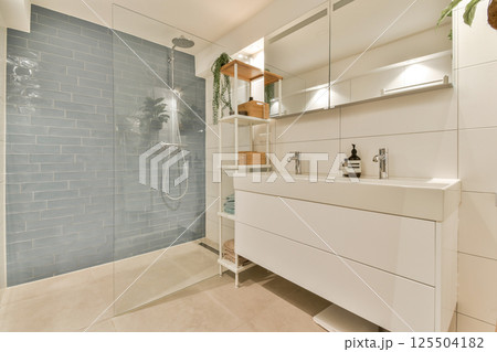 A sleek, modern bathroom featuring a walk-in shower with tiled walls, a stylish vanity, and organized shelves with decorative items and toiletries. A sleek, modern bathroom featuring a walk-in shower with tiled walls, a stylish vanity, and organized shelves with decorative items and toiletries. 125504182