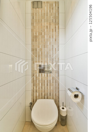 A sleek and modern bathroom showcasing neutral tones, a minimalistic design, and elegant tile work on the walls. It features a clean toilet and essential accessories. 125504196