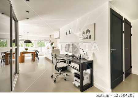 A sleek and contemporary home office featuring a desk, ergonomic chair, and stylish decor set in a bright, open space with natural lighting. 125504205