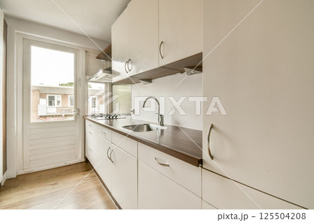 Sleek modern kitchen features minimalist cabinetry, a gas stove, and large windows offering natural light, enhancing the contemporary aesthetic. 125504208