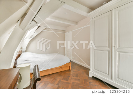 The image showcases a cozy modern bedroom with a light color palette, featuring unique architectural details and stylish furniture. The image showcases a cozy modern bedroom with a light color palette, featuring unique architectural details and stylish furniture. 125504216