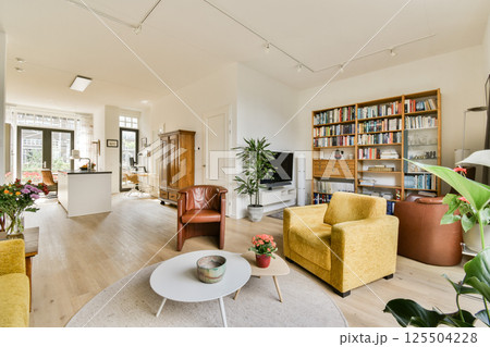 Spacious living room featuring bright furniture, bookshelves, and natural lighting, creating a warm and inviting atmosphere perfect for relaxation. 125504228