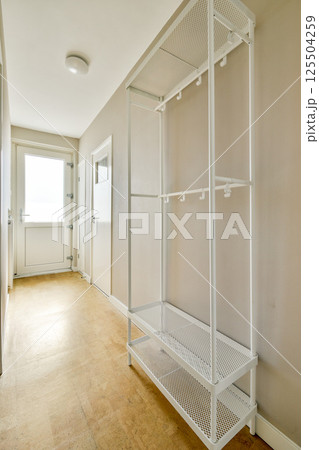 A spacious and well-lit hallway featuring a sleek metal shelving unit and light-colored walls, showcasing minimalist interior design aesthetics. A spacious and well-lit hallway featuring a sleek metal shelving unit and light-colored walls, showcasing minimalist interior design aesthetics. 125504259